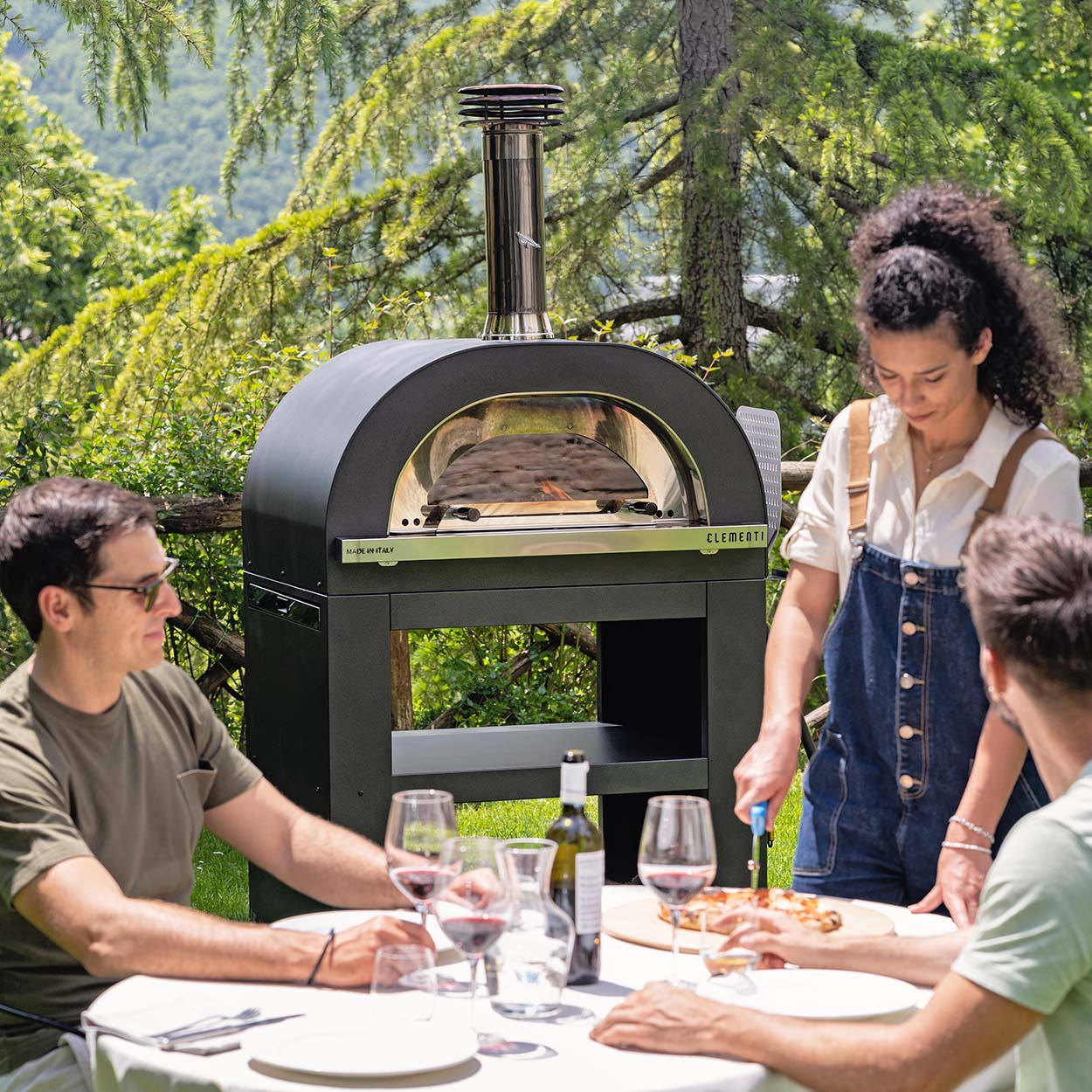 People eating pizza with Clementi Gold oven on stand in background